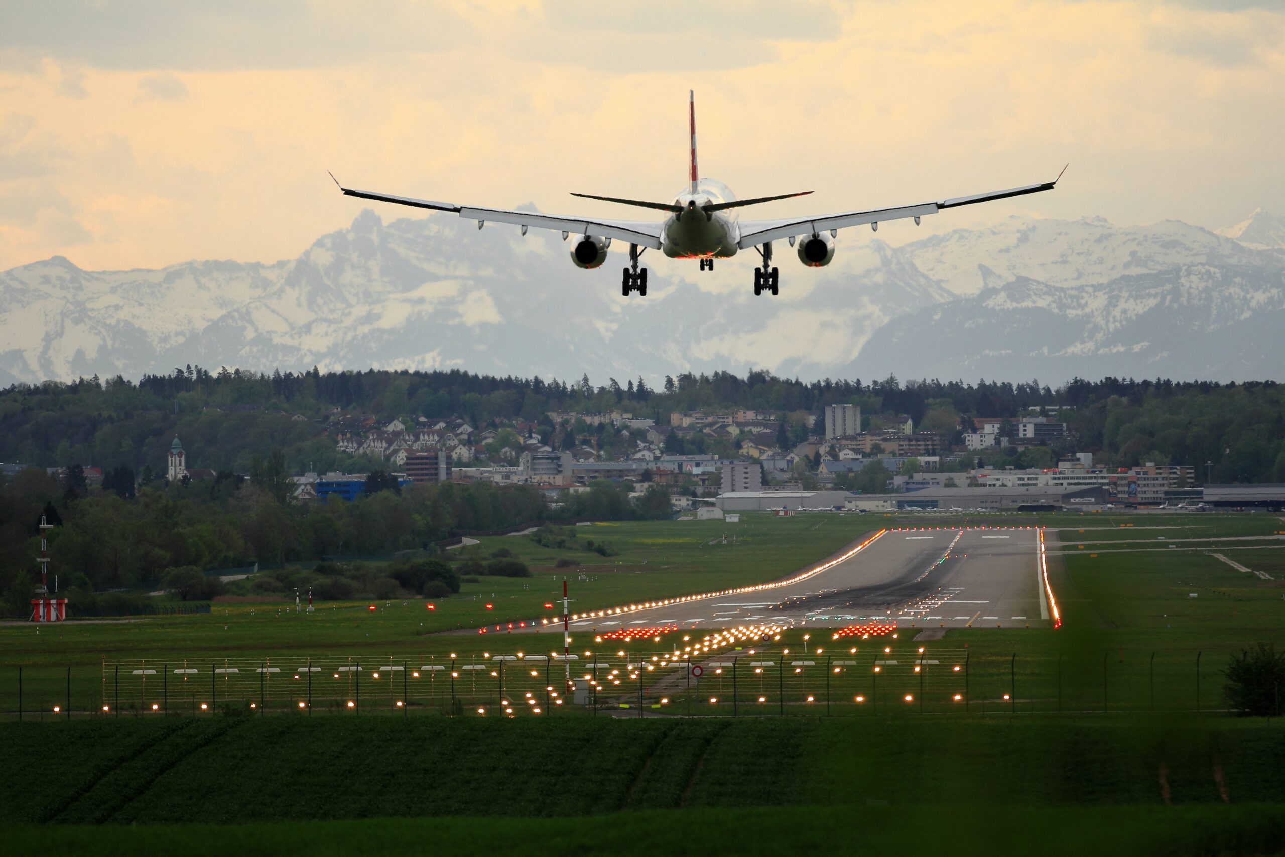 A white airplane preparing for landing on a landing strip with bright lights with mountains in the background.