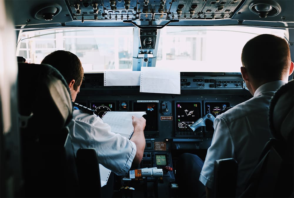 A view behind two pilots in a cockpit looking at papers and their dashboard.