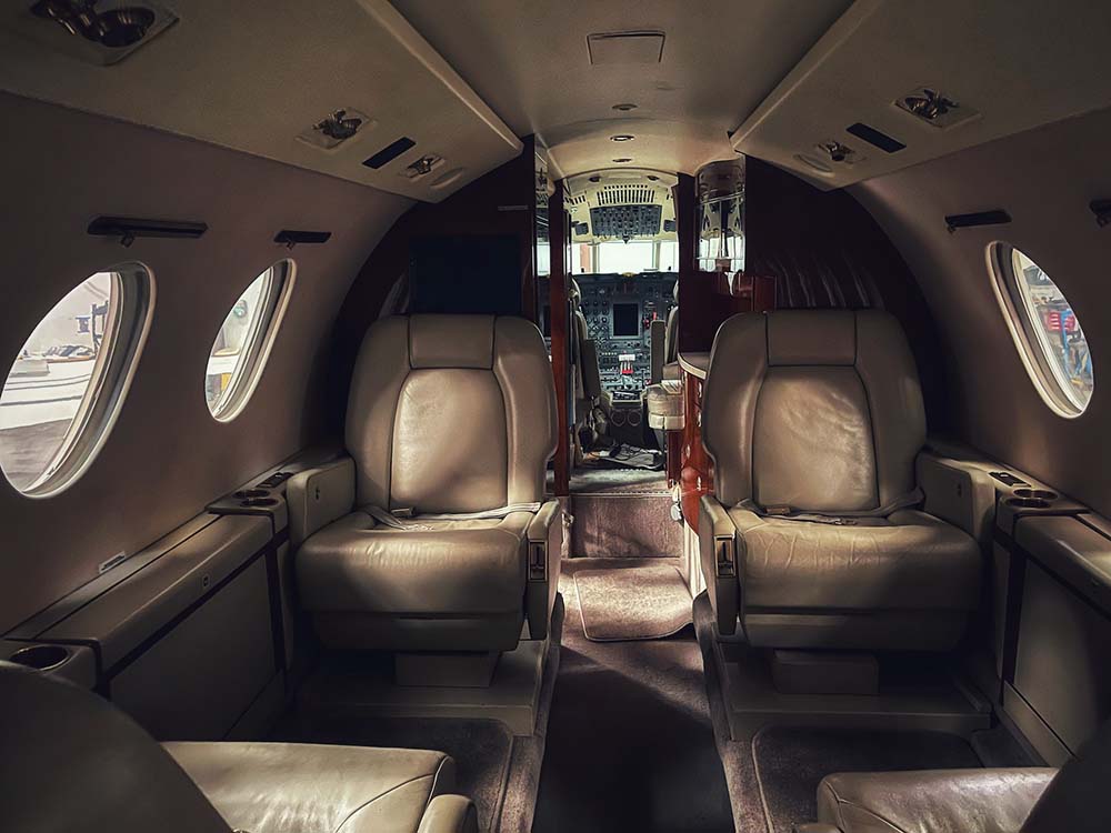 The interior of a private jet with circular windows and beige leather seats.