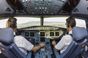 Two pilots in the cockpit of a plane, as seen from behind.